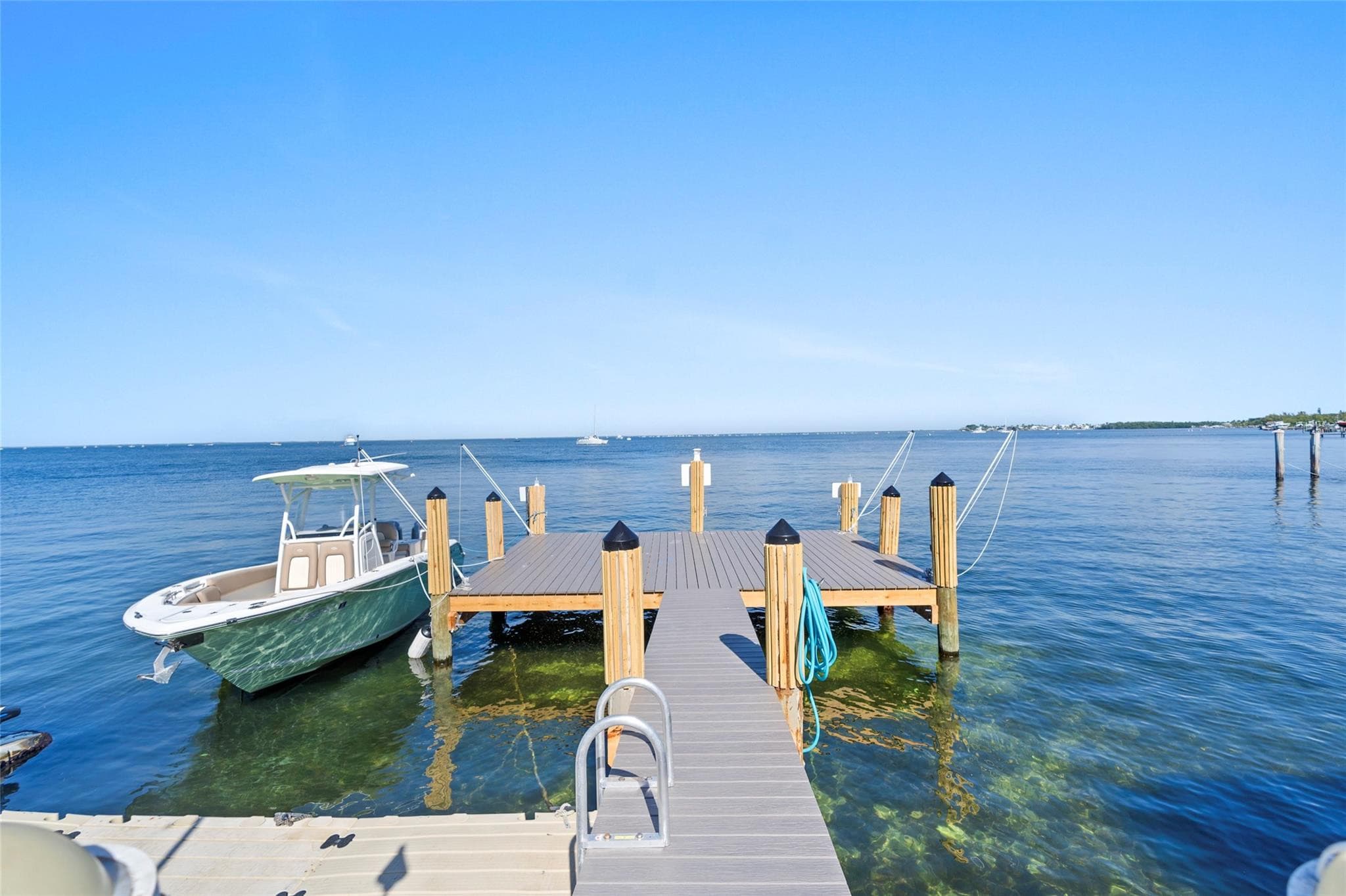 Center-console boat with a white T-top moored beside a new composite dock with wood pilings in clear, shallow turquoise water.